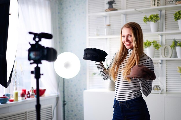 fashion blogger woman in jeans and turtleneck showing fashionable caps on camera stylist influencer girl showing trendy hats filming vlog episode for her video channel opinion leader sets trends