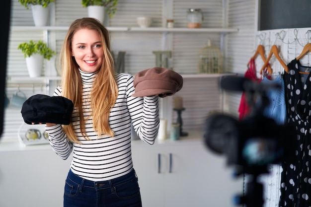 Fashion blogger woman in jeans and turtleneck showing fashionable caps on camera stylist influencer girl showing trendy hats filming vlog episode for her video channel opinion leader sets trends