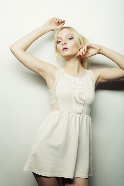 Fashion blond woman in white dress posing in studio