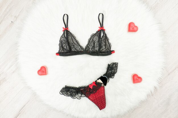 Fashion concept. black lacy bra and panties on white fur. red heartshaped candles