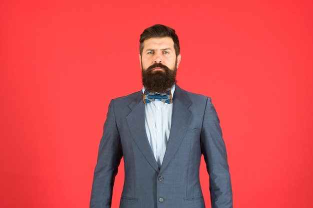 Fashion concept. businessman or host fashionable outfit red
background. formal outfit. confident posture. man bearded hipster
wear classic suit outfit. take good care of suit. elegancy and male
style.