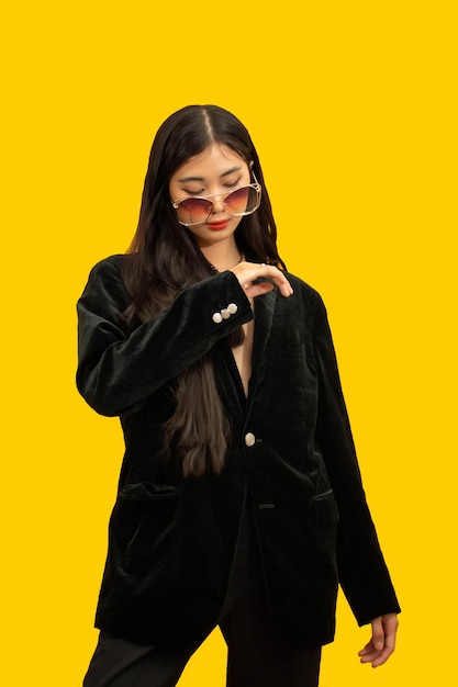 Fashion concept fashionable woman posing in a black outfits with sunglasses over yellow background