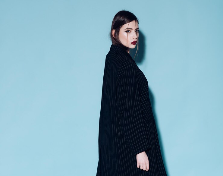 Photo ファッションコンセプト。長い黒のコート、灰色の背景で厳格な自信を持って顔の女の子。カメラを見ている赤い唇を持つ女性、コピースペース。スタイリッシュなメイクと髪型の女性。