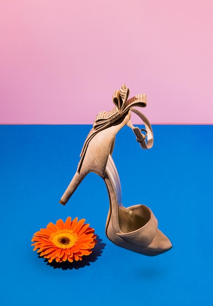 オレンジ色のデイジーの花とモダンなハイヒールの靴のファッションコンセプト創造的な重力春のアイデア