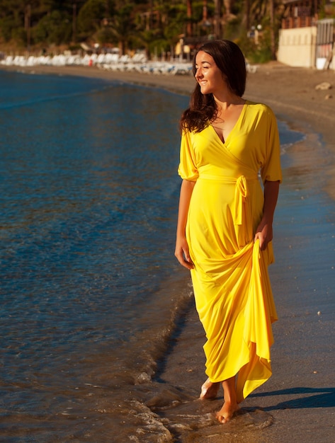 Fashion concept Woman with long yellow dress walking alone on the beach