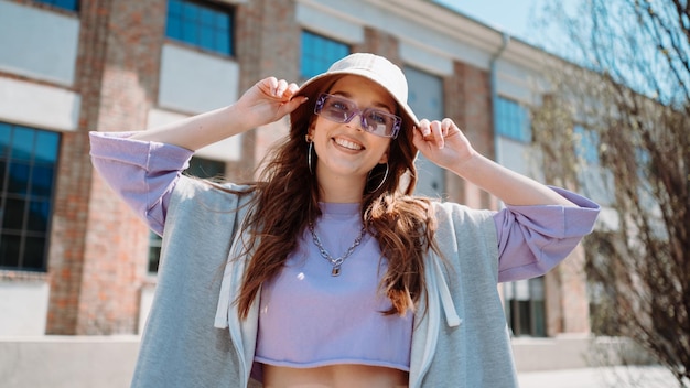 Fashion cutte woman with sunglasses and hat dancing outside looking at camera Female dancer performing dance show making freestyle stunts