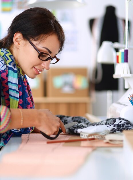 Модный дизайнер резки текстиля рядом с швейной машиной