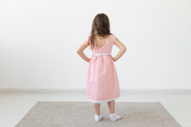 Stilista, bambini e concetto del bambino - vista posteriore della bambina che posa in vestiti allo studio