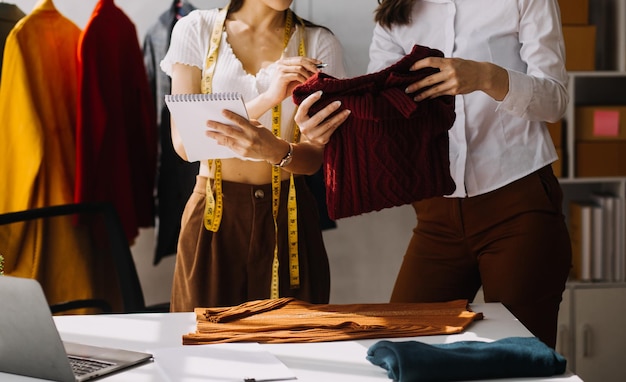 Foto stilista l giovane donna asiatica che lavora utilizzando il tablet portatile e sorride mentre si trova in officina rispondendo per affari