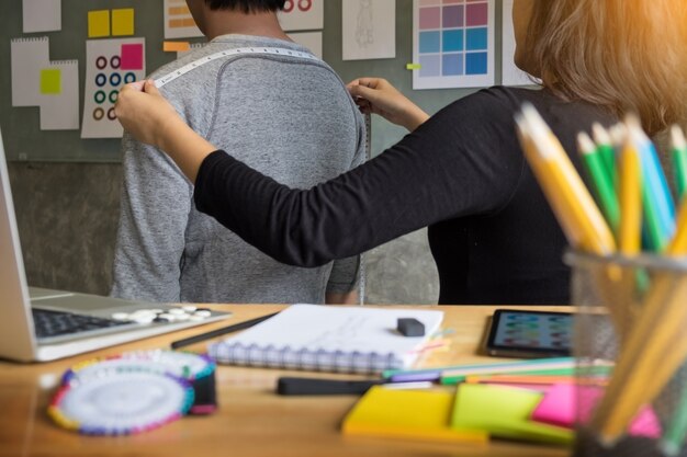 Foto designer di moda che misura sulla cassa dietro gli uomini per un vestito su misura per un giovane uomo d'affari.