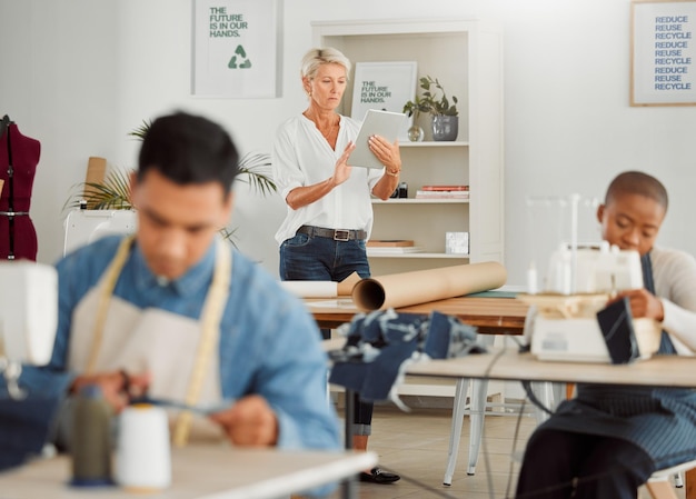 Stilista sarto e manager che legge gli ordini online su un tablet nel suo laboratorio di avvio piccola azienda di abbigliamento che gestisce il personale e i lavoratori della sua azienda di cucito