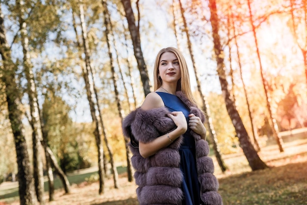 Fashion dresses woman in fur coat and dress posing in autumn park