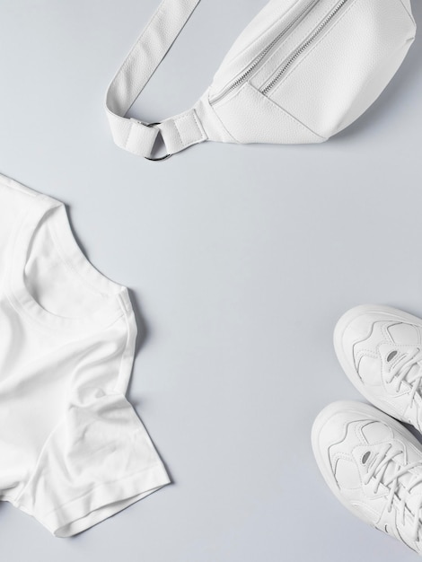 Модная плоская планировка с белой футболкой, кроссовками, поясной сумкой и аксессуарами, монохромная концепция, повседневный вид, копия пространства, вид сверху по вертикали