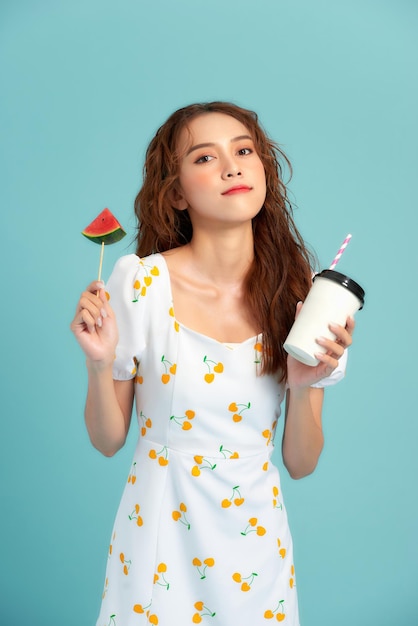 Fashion girl drinks a fruit juice from a cup holds slice of watermelon ice cream over blue background