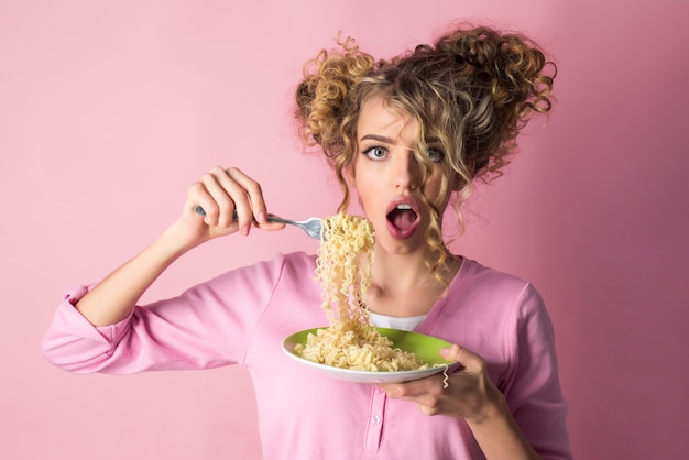 麺を食べるファッションの女の子。スパゲッティの女性ホールドプレート。朝の朝食-マカロニを食べる魅力的な女性。パスタを食べる巻き毛の愛らしい女性。ファッション、美容、ダイエット、食べ物、食事、イタリア