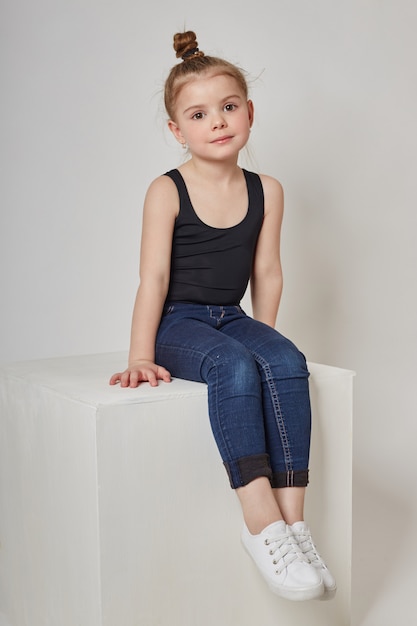 Fashion girl with long hair in casual clothes sitting on a white cube and posing