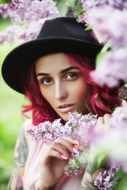 Adatti la ragazza con la vocazione dei capelli rossi, ritratto della molla nei colori lilla di estate. bellissimo abito rosa rosso, tatuaggi sul corpo di una donna. trucco luminoso, colorazione professionale dei capelli