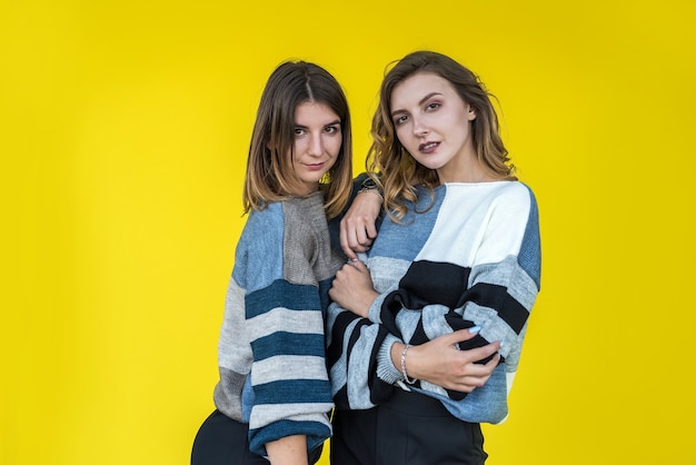 Fashion girlfriends wear modern knitted sweater posing on yellow wall