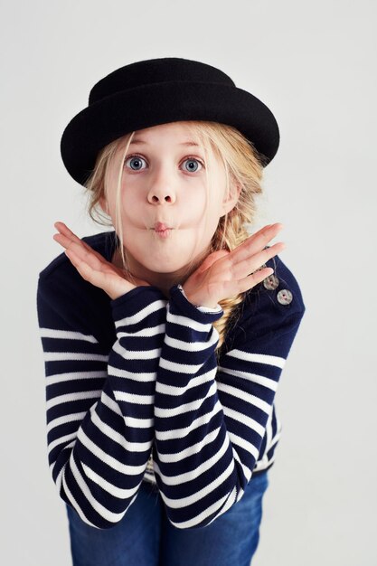 Foto fashion goofy e ragazza bambina in uno studio con casual cool e elegante jersey outfit e cappello silly comico e divertente giovane bambino modello con stile giovanile alla moda e atteggiamento positivo da sfondo grigio