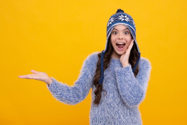 Fashion happy young woman in knitted hat and sweater having fun over colorful blue background Excited teenager girl