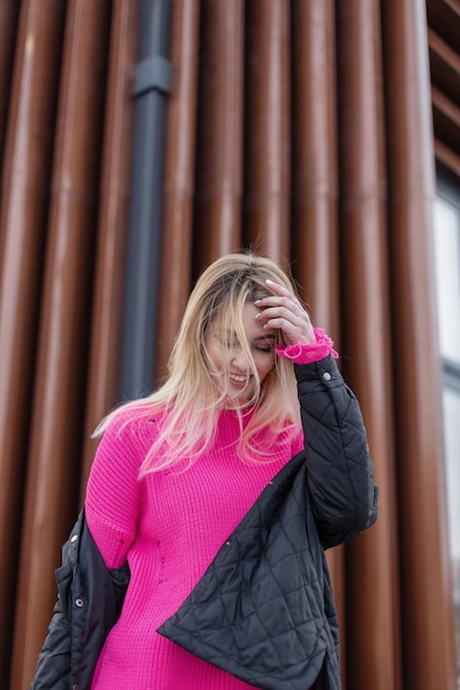 Fashion happy young woman with pink sweater and jacket walks on
the street happiness emotions