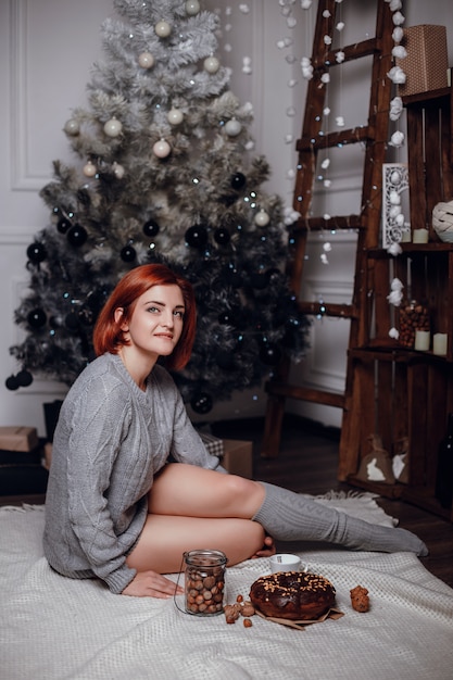 Fashion interior photo of beautiful young woman with red hair and charming smile, wears cozy knitted cardigan