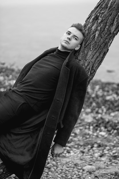 fashion male model in coat black and white photo, lies on a tree, art portrait of man