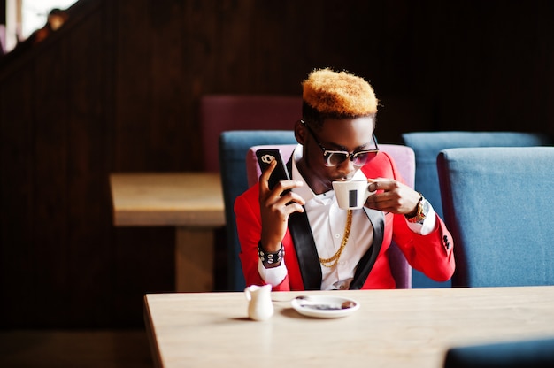 Fashion man model at red suit, with highlights hair and sunglasses sitting at cafe with coffee and speaking on mobile phone.