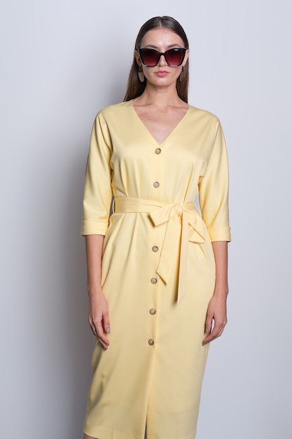 Fashion model in big sunglasses wearing yellow dress with buttons posing