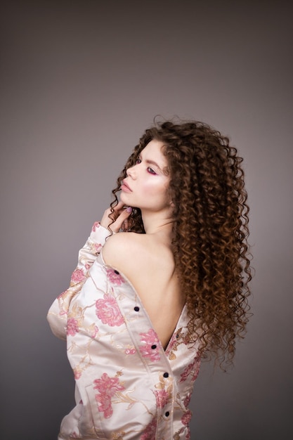 Photo fashion model girl with curly wavy shiny healthy hair on grey background hair care bright makeup