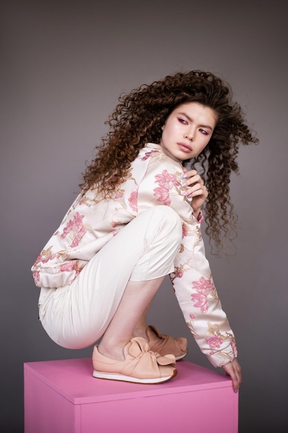 Девушка-модель с вьющимися волнистыми блестящими здоровыми волосами на сером фоне Уход за волосами яркий макияж