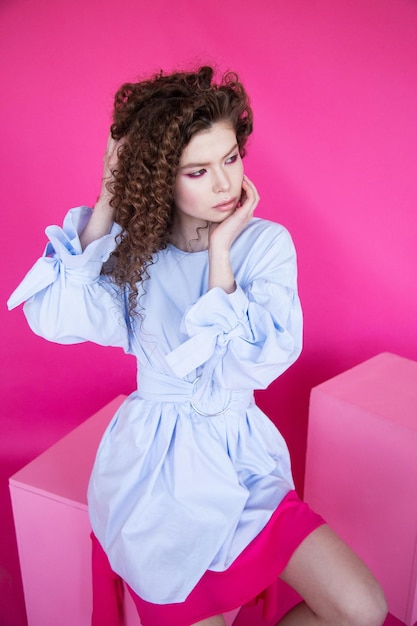 Fashion model girl with curly wavy shiny healthy hair on pink background Hair care bright makeup