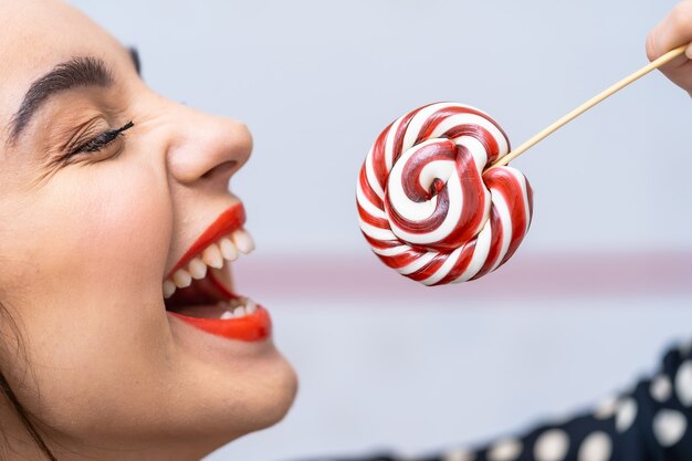 Fashion model girl with round candy in hands. Beautiful smiling young woman. Cropped photo.