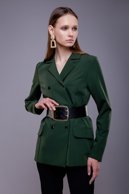 Fashion model in green suit black pants wide belt beautiful\
young woman gray background