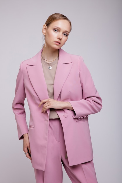 白い背景の上にポーズをとるピンクの特大のスーツのジャケットパンツのファッションモデルスタジオショット