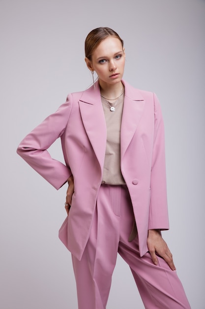 白い背景の上にポーズをとるピンクの特大のスーツのジャケットパンツのファッションモデルスタジオショット