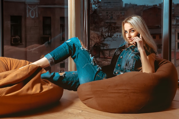 Fashion model posing on couch with mobile phone in hand and looking. Concept of relax, refreshment and leisure