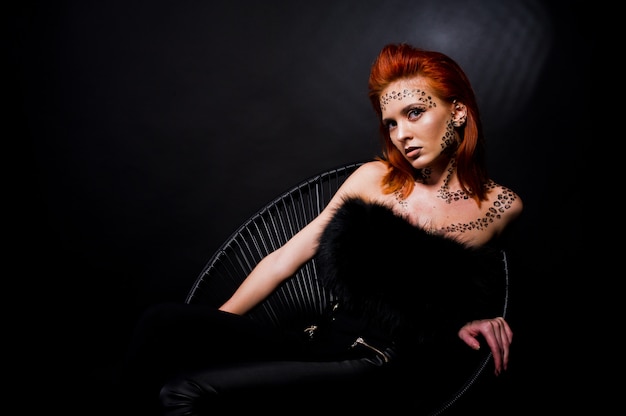 Fashion model red haired girl with originally make up like leopard predator isolated on black