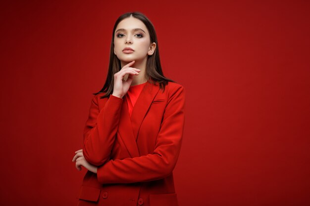 Fashion model in red suit jacket skirt Beautiful young woman Red background