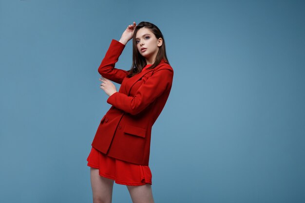 Fashion model in red suit jacket skirt Beautiful young woman Studio shot Blue background