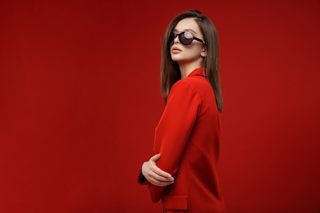 Fashion model in red suit jacket skirt sunglasses beautiful young woman red background