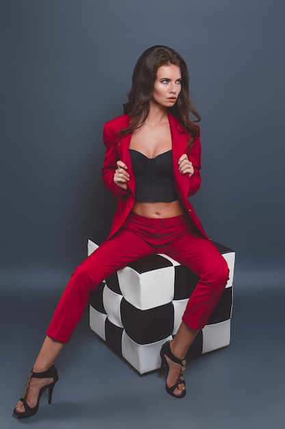 Fashion model in red suit. Young woman posing with red suit on gray