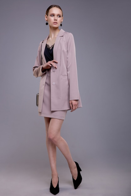 Fashion model in soft pink suit handbag beautiful young woman Studio shot Gray background