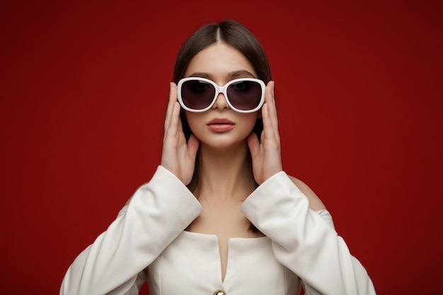 선글라스 흰색 정장에 패션 모델 아름 다운 젊은 여자 스튜디오 촬영 빨간색 배경