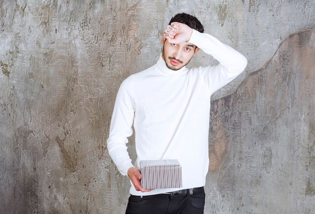 Fashion model in white sweater holding a silver gift box and looks tired.