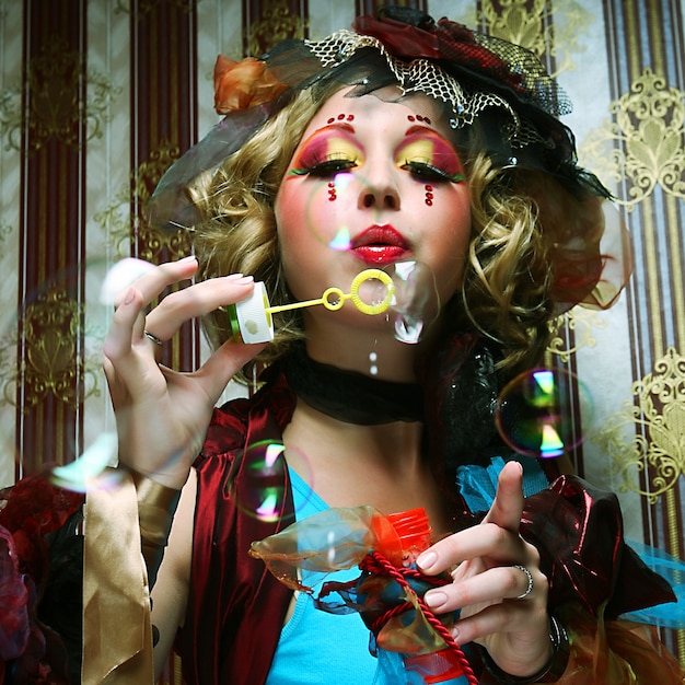 Fashion model with creative make-up blowing soap bubbles.