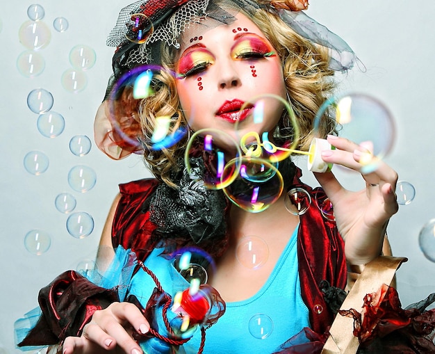 Fashion model with creative makeup blowing soap bubbles