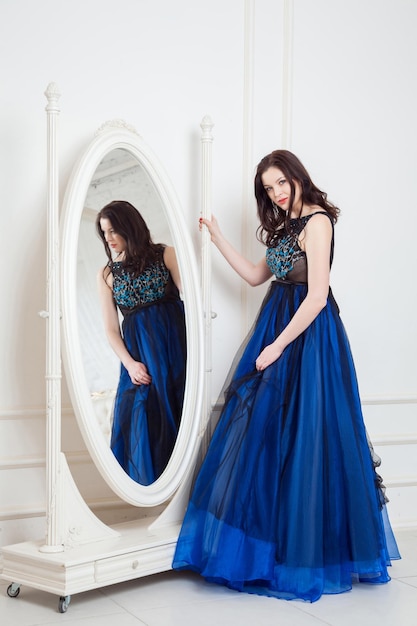 Photo fashion model with dress standing and posing near big mirror