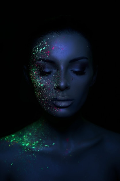 Fashion model woman in neon light bright fluorescent makeup, drop on face