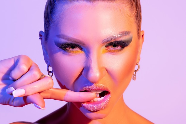 Fashion model woman with a bright make-up in colourful bright light is posing in studio.